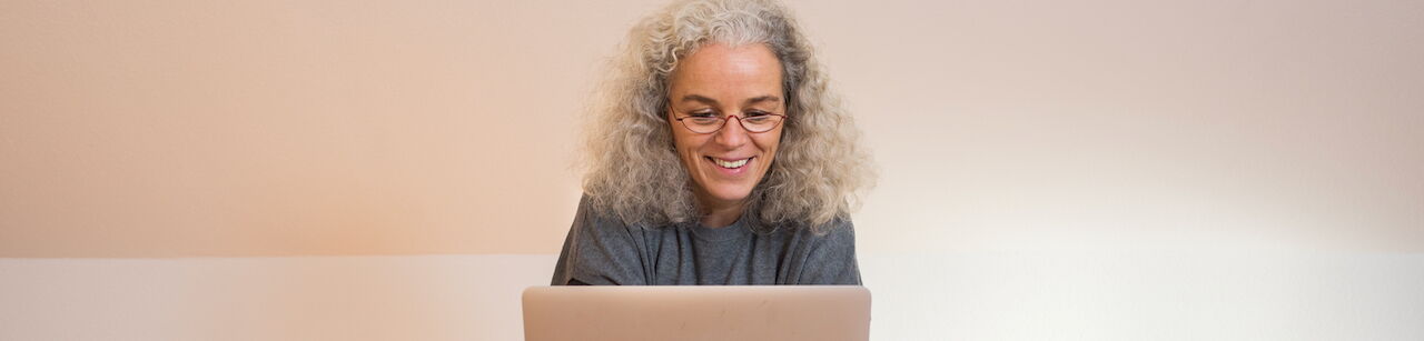 Frau mit grauen Locken, lächelnd auf ein Laptop schauend